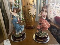Photo showing both Adeline Collection ceramic figurines on a table next to a large floral vase and chairs, displaying the overall appearance and scale