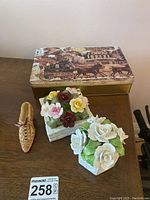 Lot of floral ceramic decorations, miniature shoe, and cookie tin arranged on a wooden surface