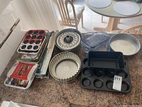 All bakeware items shown on kitchen counter including metal bundt pan, cupcake pan, springform pan, loaf pans, aluminum foil trays, and glass baking dishes.