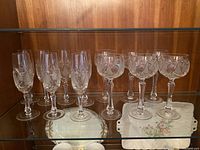 Group photo of 5 crystal flutes and 5 crystal red wine glasses on glass shelf with wood background