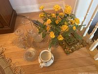Collection of clear glassware including punch bowl, glasses, clear glass bowls, and porcelain Royal Albert teapot body without lid, all on hardwood floor near staircase.