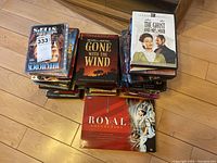 Wide view of three stacks of assorted DVDs on wooden floor including classic film titles and a large red boxed 'Royal Collection' by BBC.