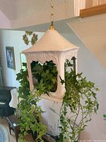 White ceramic hanging planter box with trailing faux ivy plant inside, hanging near staircase.