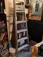 Full view of the 6 ft aluminum painting ladder leaning against wall in basement with bookshelves and electrical panel nearby.