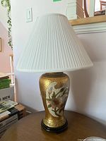 Full view of lamp with white pleated lamp shade and detailed floral design on gold crackled base.