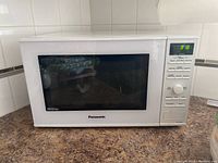 Side angle view of white Panasonic inverter microwave oven on countertop showing digital clock display active at 3:18 and control panel on right side.