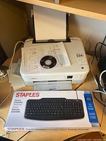Canon Pixma TS5300 printer with paper loaded, installation CD on top, and Staples keyboard box in foreground