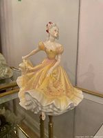Front and side view of the Royal Doulton HN2379 Ninette figurine on a glass shelf.