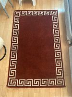Full view of the rectangular area rug showing the deep reddish-brown color with a white Greek key border design.