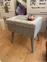 Photo of vintage floral covered sewing box on blue tapered legs with yellow feet caps, pincushion on top with pins.