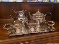 Full view of the Canadian silver plated tea service set including teapot, sugar bowl, creamer, serving tray and pitcher on wooden background.