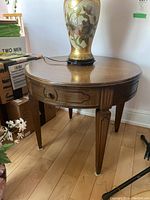 Full view of the round wooden end table showing the drawer, tapered legs, and wood finish.