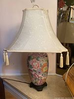 Full view of ceramic table lamp showing floral patterned base, fabric shade with tassels, and wooden stand.