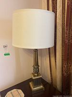 Full view of one brass table lamp with white drum shade on a table, showing overall shape and design
