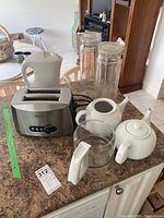 Photo showing all items including two white ceramic teapots, two glass pasta storage jars, stainless steel toaster and white electric kettle arranged on counter