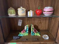 Front view of ceramic trinket boxes, floral bookends, and paperweights displayed on a wooden shelf