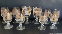 Photo of 10 vintage Libbey champagne glasses with gold leaf decoration arranged in two rows, showing variation in size.
