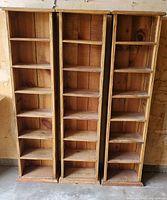 Photo showing three identical vertical wooden media storage shelves with six compartments each.