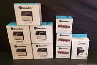 Photo showing stacked boxes of Boundery LumiGuard PRO solar lights in original packaging, total 9 boxes visible including different variations.