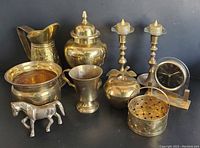 Full lot showing all 10 brass items including candlesticks, ginger jar, pitcher, basket, horse figurine, clock, lidded apple, goblet, and bowl.