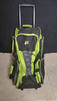Front and handle view of black and lime green Fila rolling duffle bag showing multiple zippered compartments, elastic cording, and logo.