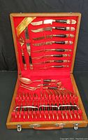 Full view of Johnny's Gems gold tone silverware set inside wooden case with red lining, showing knives, forks, spoons, and specialty utensils in neat arrangement.