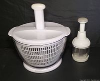 KitchenAid white salad spinner with colander basket beside Pampered Chef manual chopper with transparent base and white handle.