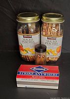 Two large glass jars filled with wooden stick matches, two with Kirkland Sliced Peaches label, one smaller container of matches, and a box of Diamond brand strike anywhere matches.