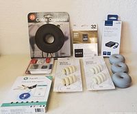 Lot showing black XL cable organizer, Sony 32GB SDHC UHS-I memory card, Insignia USB to VGA adapter, three gray cable organizers, two white wire snake cable holders, and TrackR pixel key tracker in original packaging.