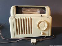Full view of vintage Mitchell Lullaby bed radio showing overall shape, beige casing, top bulb window, and front speaker grille with original cord and plug.