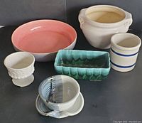 Overview of six vintage pottery items on dark surface showing bowl, planters, crocks.