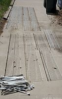 Top-down photo showing wire shelving panels of various lengths laid out on pavement, including several very long panels approximately 143 inches long and 12 inches wide.