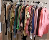 Full view of the women's clothing on rack showing assortment of jackets, tops, skirts, and dresses in various colors including a notable pink jacket on the right side.