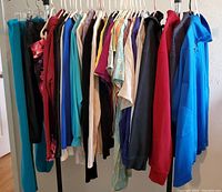 Lot of women's clothing hanging on rack showing variety of colors and styles including pants, casual and business tops, hoodies.