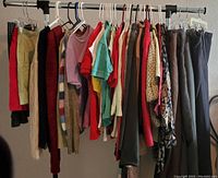 Front view of the lot showing women's clothing hanging on a rack including wool dress pants, sweaters, tops, and business jackets in various colors, mostly neutral with some brighter colors.
