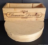 Photo showing the top view and side of the round wooden cheese box and rectangular Domaine Drouhin wine crate stacked together, highlighting their size and rustic wood finish.