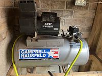 Front angle view of Campbell Hausfeld air compressor tank and motor unit with branding and yellow air hose attached.