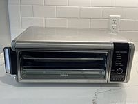 Front view of Ninja countertop air fryer with closed glass door and control panel visible.