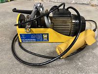 Side view of yellow and black PowerFist electric cable hoist with attached cables and yellow control switch.
