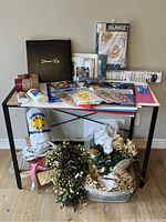 Lot of crafting items displayed on table and floor including ribbons, glue, frames, stickers, cardstock and artificial flowers.