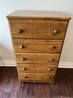 Front view of tall wooden dresser with five drawers and round wooden knobs