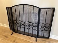 Full view of the black metal fireplace screen with arched top and decorative scrollwork, showing folding side panels partially open.