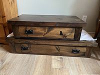 Two wall mounted floating bedside tables stacked, showing dark stain rustic pine wood with drawers and metal handles, one broken