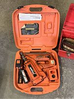 Orange Paslode framing nailer in plastic case with charger and manual visible