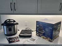 Photo showing Instant Pot Duo, Salton induction cooktop, Rival chocolate fountain box, and user manuals on a kitchen counter.