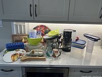 Wide shot of the countertop showing all kitchen items including coffee maker, bowls, plates, and containers.