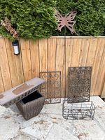 All items displayed outside against wooden fence: wicker-look planter box, butterfly stake, two decorative metal panels, wire planter basket