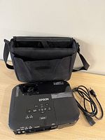 Top view showing Epson EX5210 projector with buttons, ports, power cord and carrying case behind it.