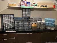 Wide view of stock storage bins and containers filled with mixed screws, nails, washers, plugs, clips on black countertop.