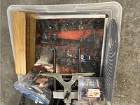 Top-down view showing a plastic bin with router accessories including bits, metal guides, and wooden elements.